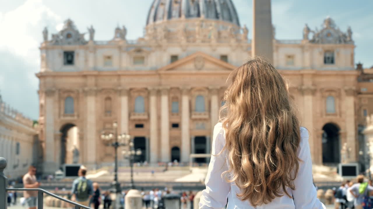 Visuale da dietro di una donna bionda nella Città del Vaticano. Piazza San Pietro con numerosi turisti, Basilica di San Pietro e l'obelisco vaticano sullo sfondo. Rallentatore