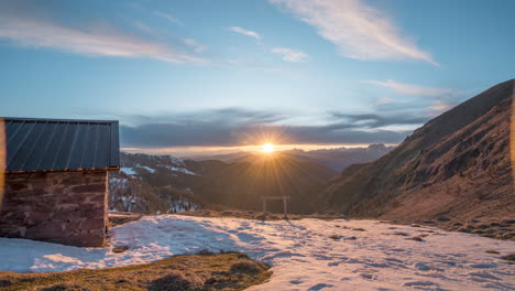 Berghütte-Bei-Sonnenaufgang-Mit-Schneebedeckten-Gipfeln-Und-Solarpaneldach,-Weitwinkel-Zeitraffer