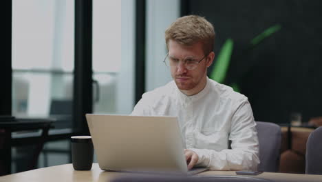 focused young man wearing glasses using laptop typing on keyboard writing email or message chatting shopping successful freelancer working online on compute