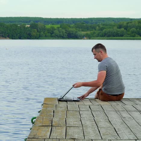 man with his notebook is working outdoor at the lake. old wooden pier