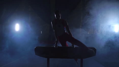 male gymnast athlete performs handstand and rotation on pommel horse on dark background and smoke in slow motion