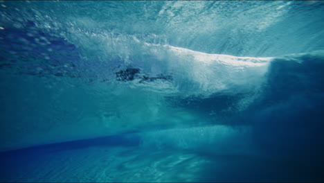 slow motion underwater shot of waves building up in artificial wavepool, light reflects dynamically in the water, dreamy surfer silhouette