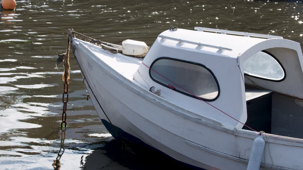 White motorboat anchored, gently rocking on sunlit water, Loch Brandy, daylight, steady close-up shot