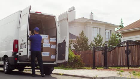 Vista-Trasera-De-Un-Repartidor-Recogiendo-Cajas-De-Cartón-De-Una-Furgoneta-En-La-Calle