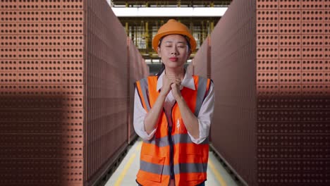 Asian Female Engineer With Safety Helmet Pray For Something While Standing With Red Brick Packed in Stacks Are Stored