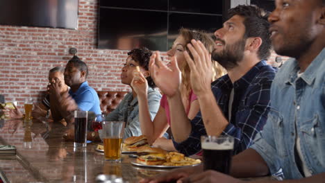 group of friends watching game in sports bar on screens