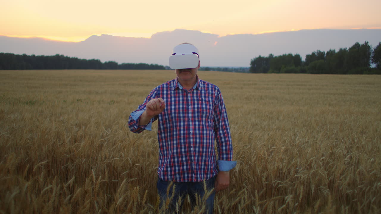 una granja anciana usa un casco vr mientras está de pie en un campo al atardecer. usar gestos para la realidad virtual en la agricultura.