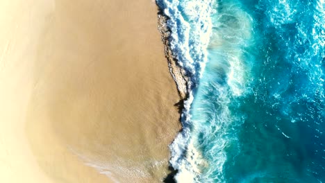 aerial view waves break on white sand beach.