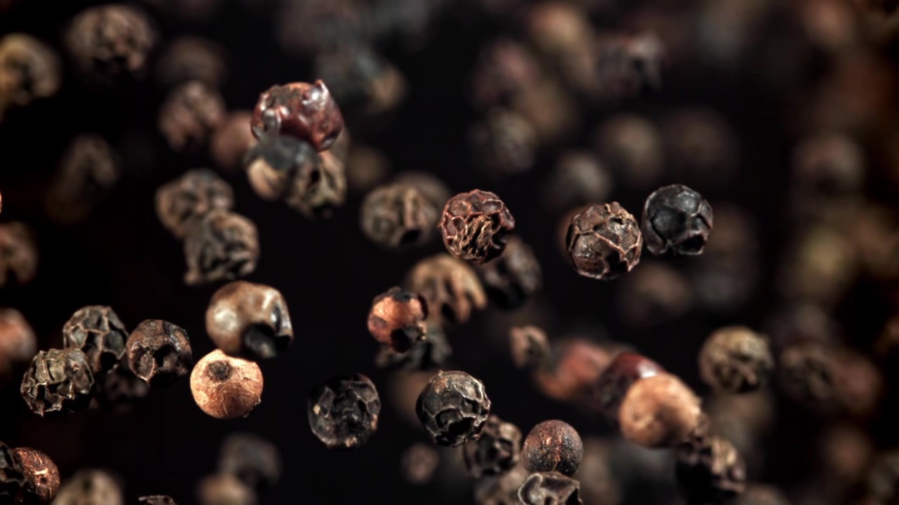 Super sakte film av svarte pepperkorn som faller og kommer i fokus
