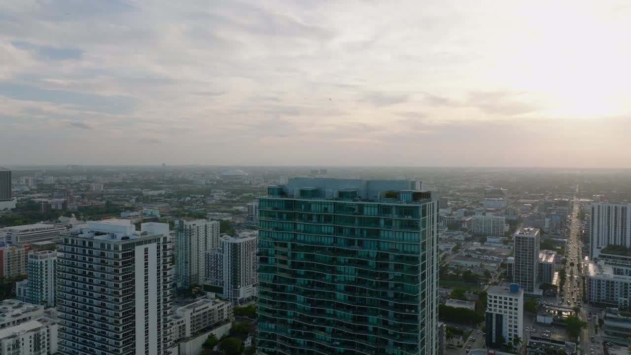 Voo sobre edifício moderno de arranha-céus na cidade. Revelando vista panorâmica de bairro residencial urbano ao pôr do sol. Miami, EUA