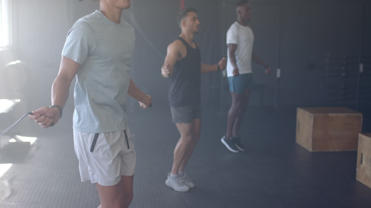 Group of diverse men training with jump ropes in gym, wearing athletic clothing