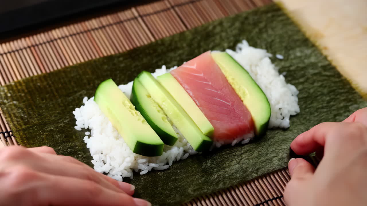 Hands rolling sushi with salmon and cucumber on a bamboo mat