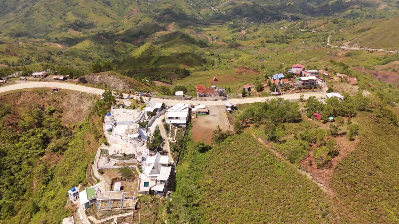 4K drone shot of a hilltop village in the Philippines, showing winding roads, green mountains, and rural buildings under bright daylight with smooth cinematic aerial motion