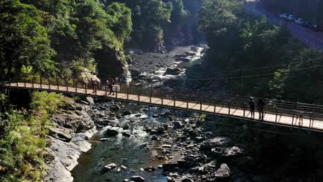 people crossing wooden bridge in green mountains of wulai district in taiwan during sunlight