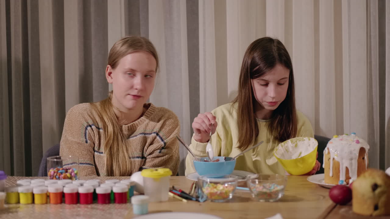 сестры украшают пасхальные яйца и лакомства.
