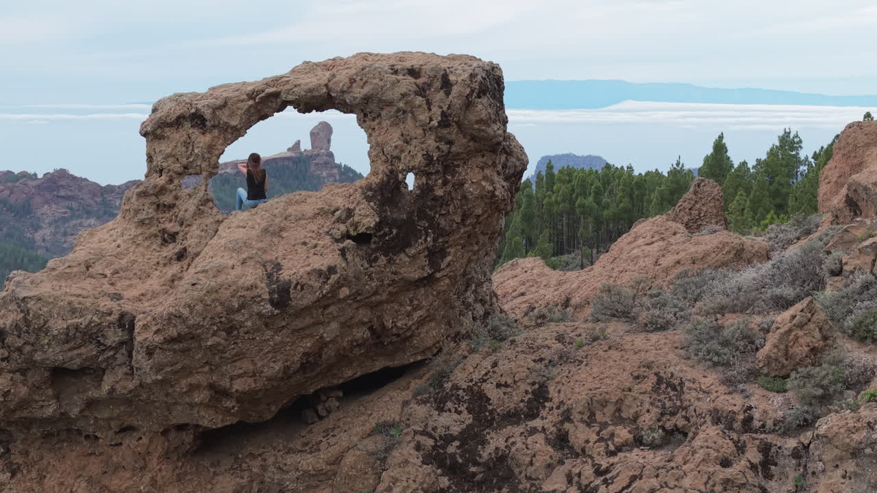Aerial video capturing a woman sitting at the Window of Roque Nublo, admiring the volcanic landscape. Gran Canaria, Spain.