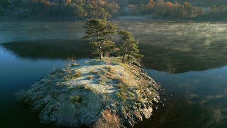 slow orbit of rocky outcrop in lake as mist flows around the island at sunrise in autumn