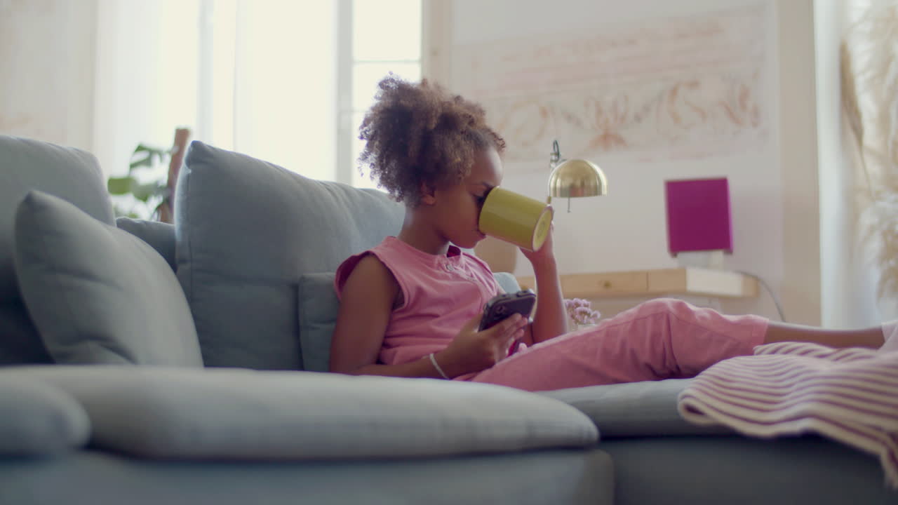 linda chica negra bebiendo té y mirando la pantalla del teléfono móvil