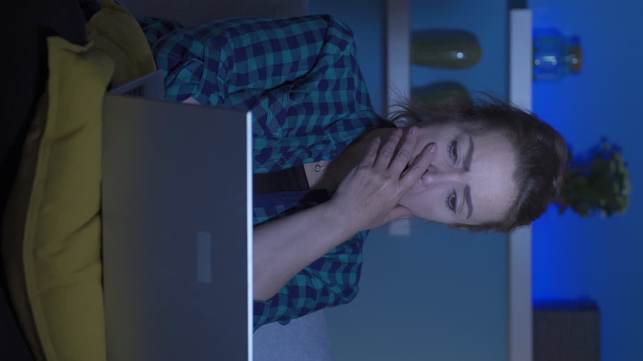 video vertical de una mujer viendo una película en una computadora portátil por la noche.