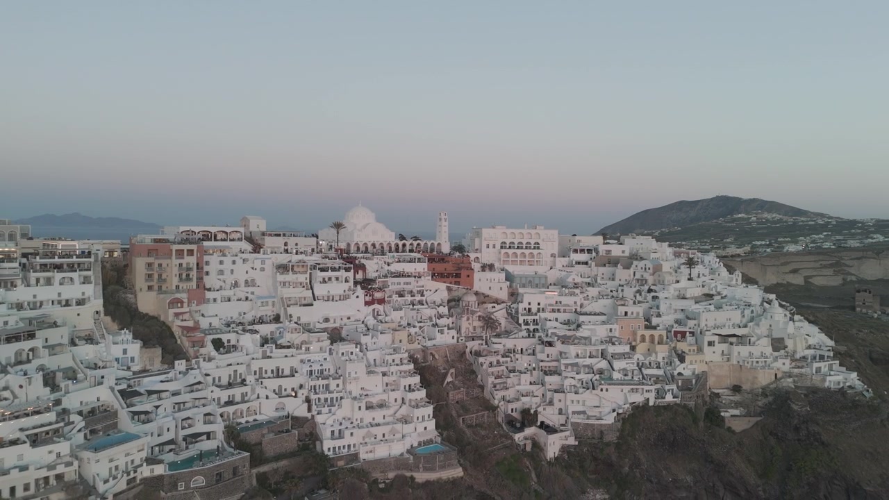 Panorâmica aérea deslizante revelando as casas brancas e vilas em Fira, Ilha de Santorini, Grécia. Cidade de Thira. Mar Egeu, Mediterrâneo