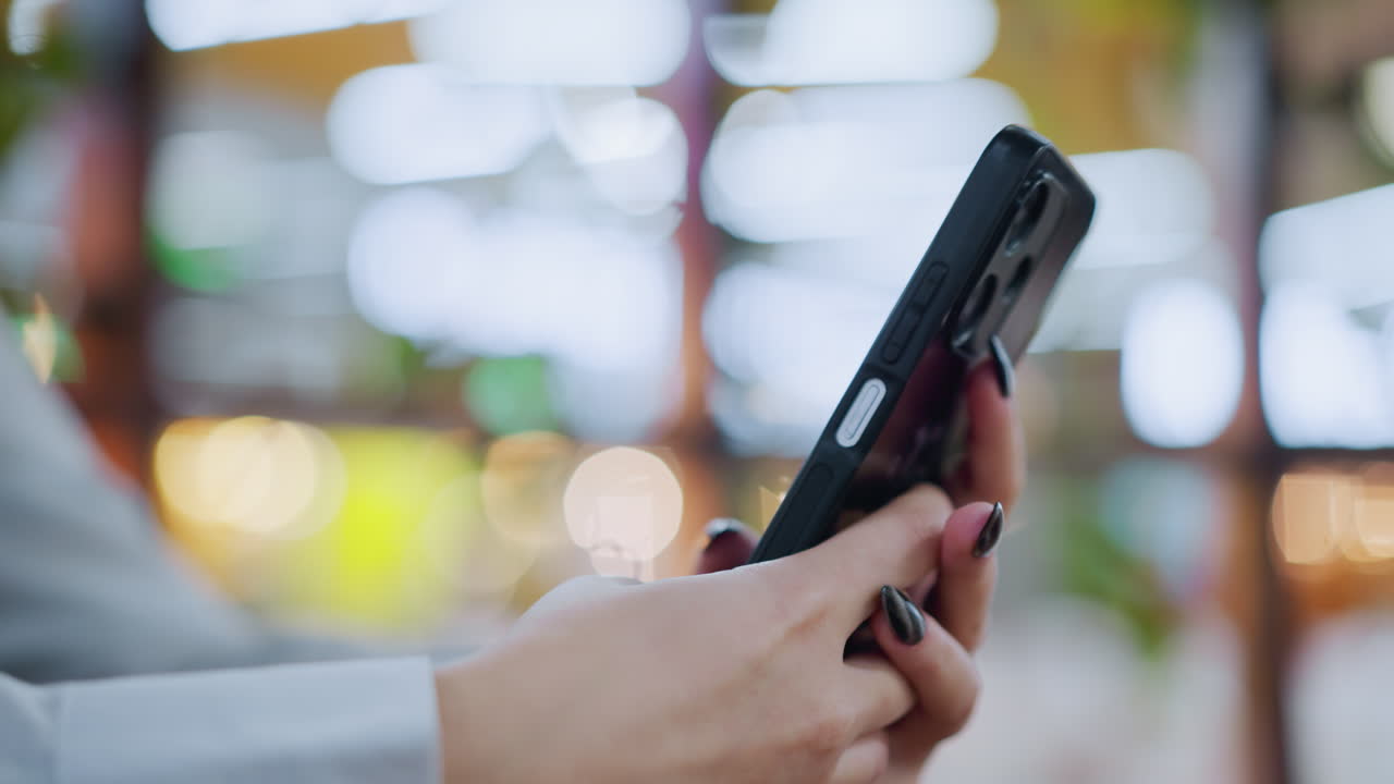 검은색 린 손을 가진 여성 손이 부드럽고 활기차고 흐릿한 배경과 보케 빛으로 전화로 대화하는 클로즈업, 스타일리시한 설정에서 의사 소통의 순간을 포착합니다.