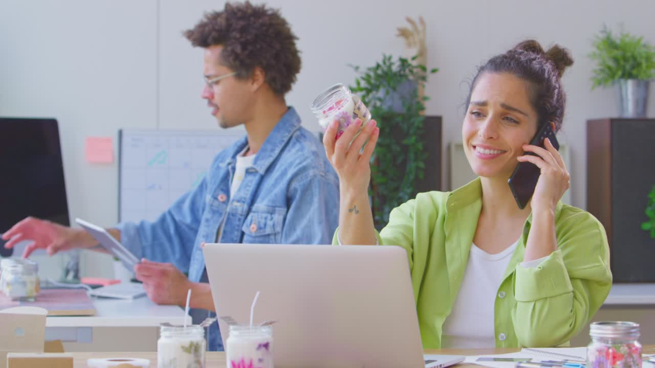 una pareja que dirige un negocio en línea haciendo velas boutique en casa usando portátil, tableta digital y hablando en teléfono móvil - filmado en cámara lenta