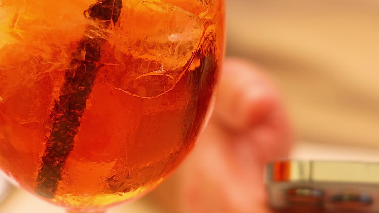 A detailed view of an orange beverage with ice and a smartphone nearby.
