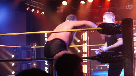 a wrestler striking his opponent by the head against the turnbuckle. the intense stage lighting and audience energy amplify the dramatic moment in the wrestling ring