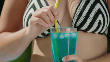 attractive woman in bikini shatters ice in a cocktail, close-up shot.