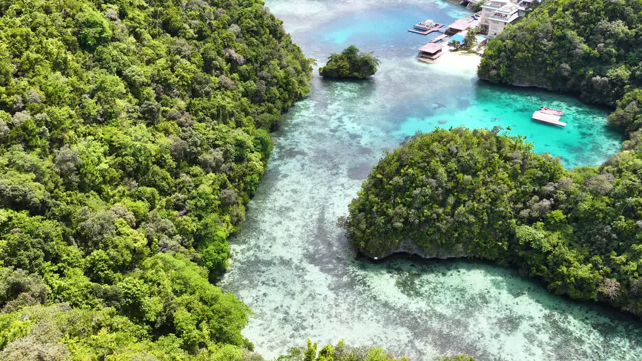 Una ripresa aerea con drone rivela un catamarano bianco ancorato nelle acque limpide di una laguna tropicale.