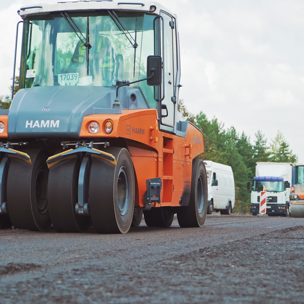 Orange roller machine pressing hot asphalt on the road. Two compactor machines are making new asphalt on the background of traffic movement. Street resurfacing.
