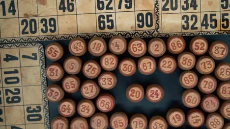 primer plano cinematográfico suave disparo desde arriba de una pila de barriles de madera de bingo en un cuadrado, figuras de madera, viejos números de fondo, juego de mesa vintage, cámara lenta 120 fps gimbal comercial inclinarse hacia abajo