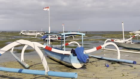 traditional indonesian jukung fishing boats sit on the sand with their outriggers extended as the tide goes out for the day