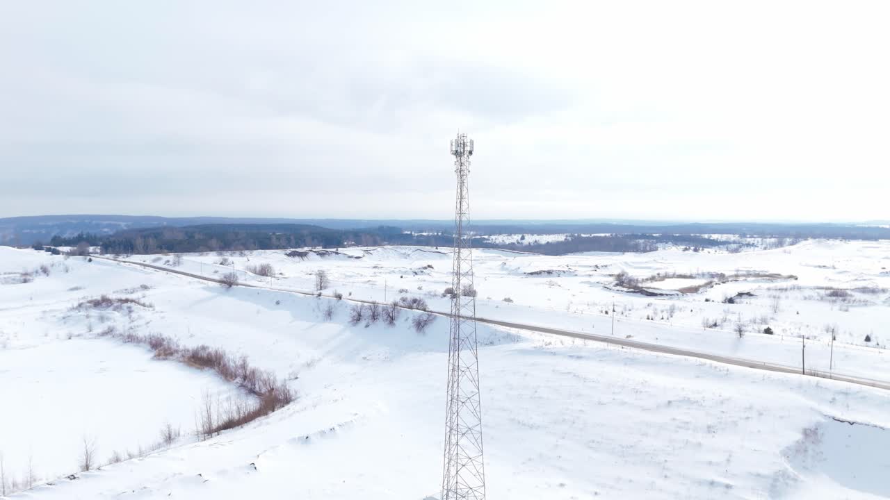 Panoramica aerea bassa attorno a una torre di telecomunicazioni in un paesaggio innevato