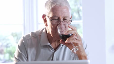 Senior-man-using-laptop-and-drinking-red-wine