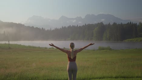 태양 인사 요가 포즈의 여성은 독일의 해가 뜨는 동안 안개가 가득한 wagenbrüchsee 호수를 바라보고 있습니다.