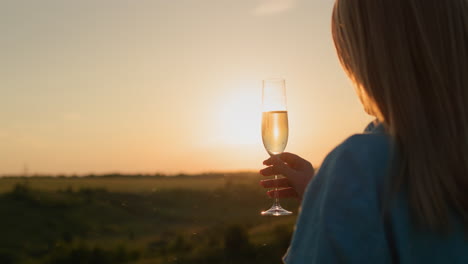 back view: successful woman with a glass of champagne on the background of a picturesque valley at sunset