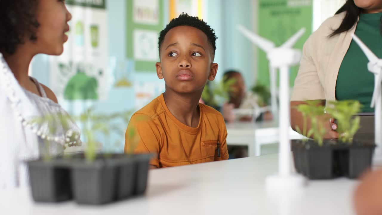 Classroom seeing left girl explaining plants, African American boy turning, listening by turbine