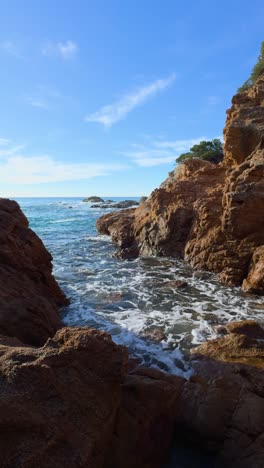 ocean waves gently crash against red rocks on a sunny day