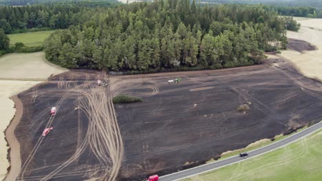 blackened remains of a fire damaged wheat field as firefighters depart
