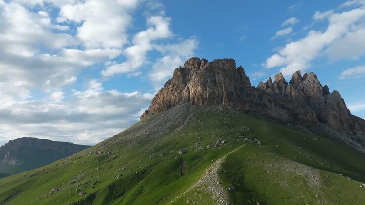 Malerische Sommerlandschaft des Naudzhidza-Berges mit zerklüftetem Felsgipfel und grünen Almhängen unter dramatischen Wolken, Russland, Weitblick ideal für Reise- und Naturthemen