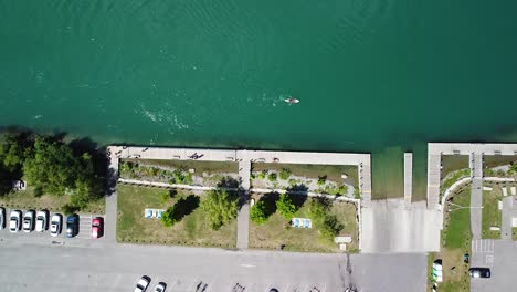 aerial top down shot of parking cars beside river with person paddling on sup board during sunny day in canada