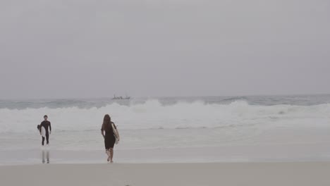 two surfers walking towards the ocean on an overcast day