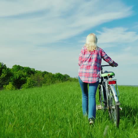 A-Woman-With-A-Bicycle-Walks-In-A-Picturesque-Place---A-Green-Meadow-And-A-Bright-Blue-Sky