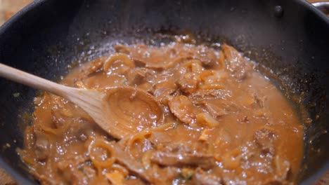 primer plano de un enorme wok mientras cocina estofado de ternera salteado con cebolla, salsa de soja y cilantro en una salsa marrón claro