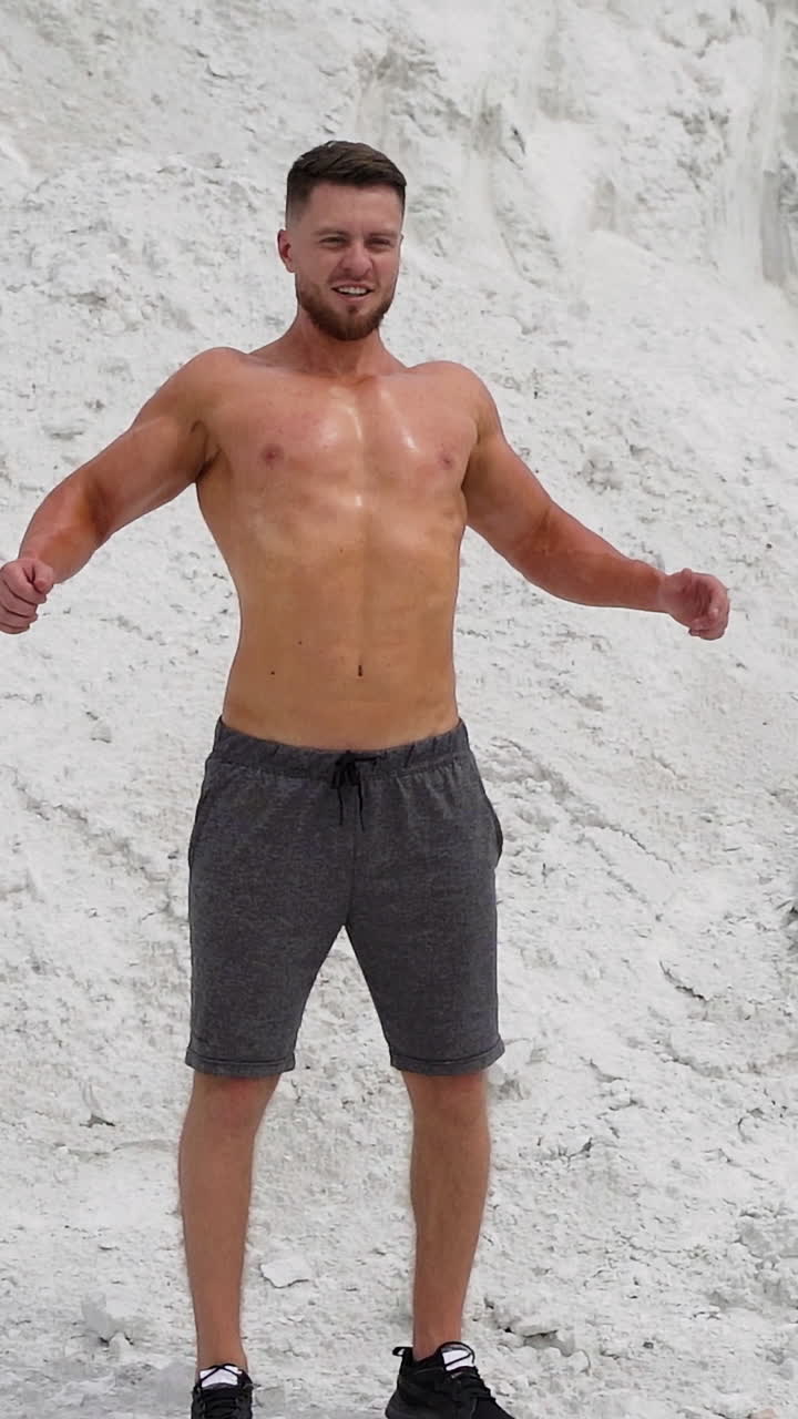 Bearded man with muscular body poses on white mountain background. Strong bodybuilder outdoors in summer. Vertical video