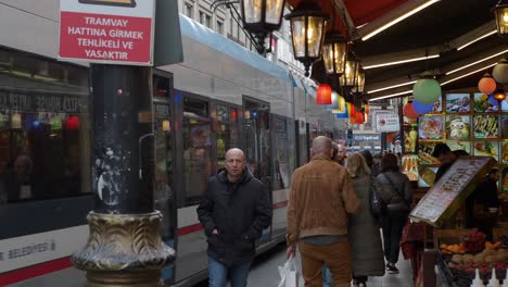 people walk by a street food stall in istanbul, turkey, with a tram in the background.