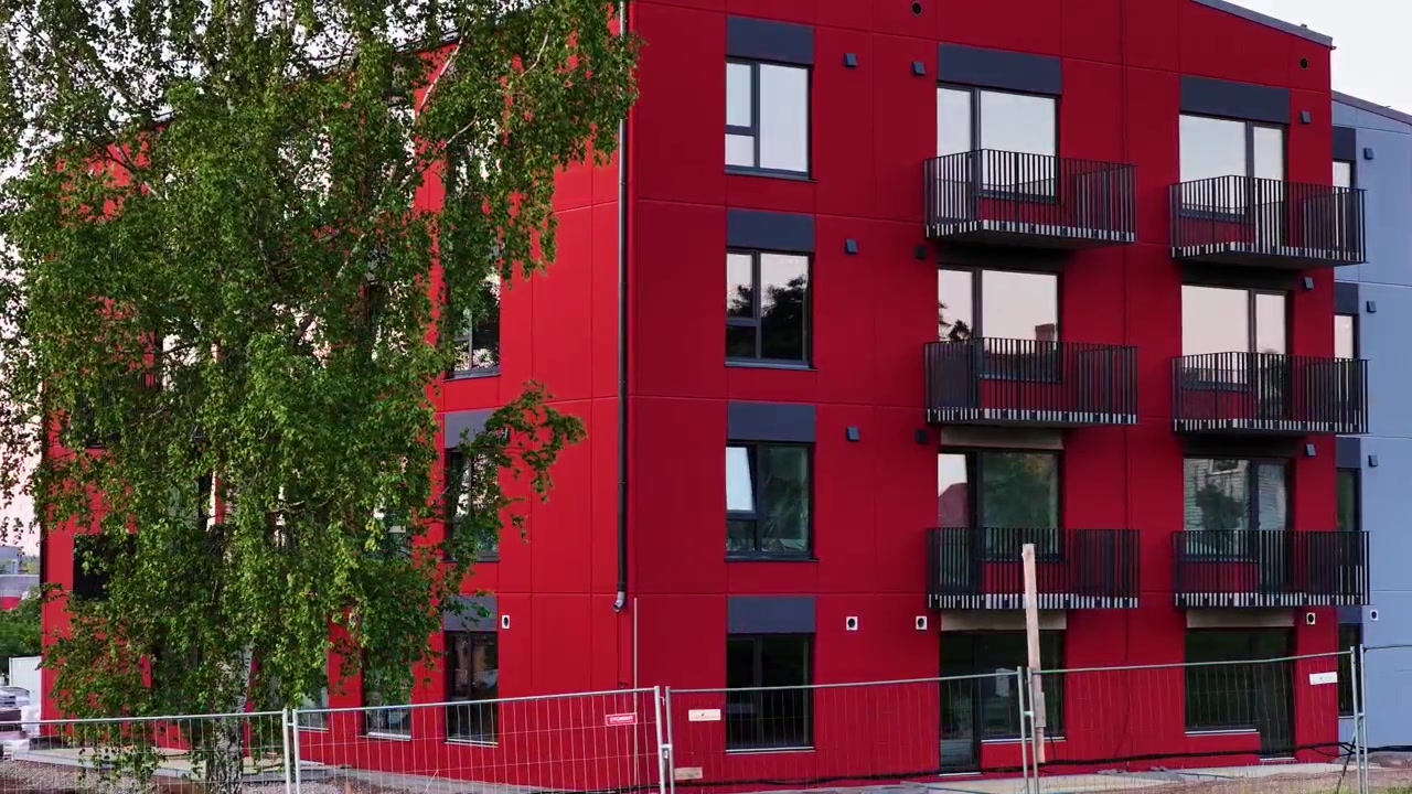 Edificio residencial rojo recién construido con arquitectura moderna detrás de una valla de construcción