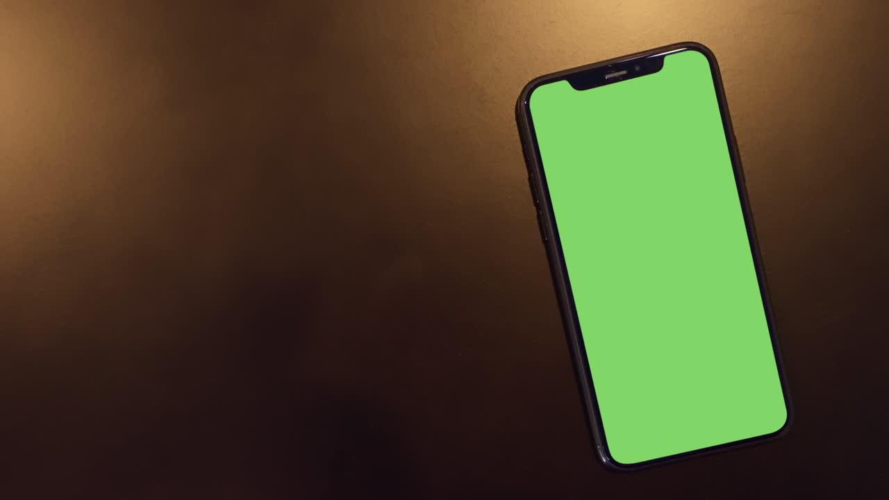 lugar de teléfono inteligente en fondo negro con luz dorada, teléfono de pantalla verde, teléfono móvil de pantalla cerrada con maqueta, monitor de tecla de croma, teléfono de llamada de primer plano, cámara lenta vista superior portátil.