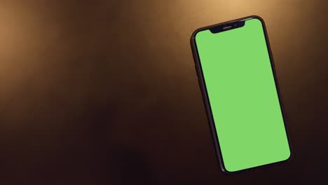 smartphone place on black background with gold light, green screen telephone, close up display mobile phone with mockup, chroma key monitor, close-up call phone, slow motion handheld top view.